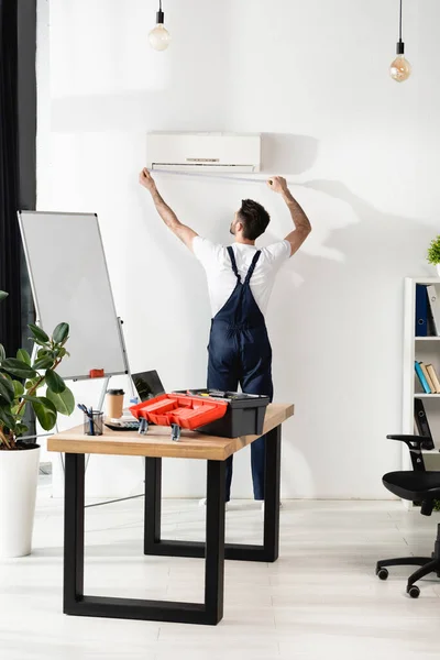 Back view of repairman measuring air conditioner on wall in office — Stock Photo