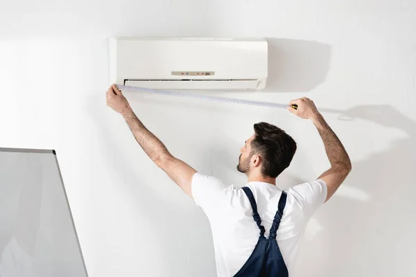 Jovem reparador de medição de ar condicionado fixado na parede branca no escritório — Fotografia de Stock
