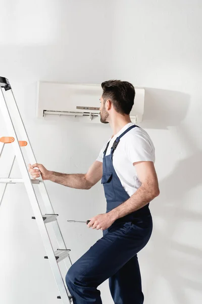 Arbeiter hält Schraubenzieher fest, während er auf Leiter neben Klimaanlage steht — Stockfoto