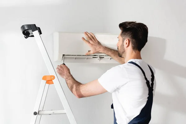 Young repairman standing on stepladder and fixing air conditioner — Stock Photo