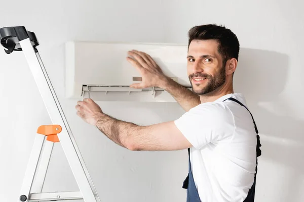 Glücklicher Arbeiter lächelt in die Kamera, während er Klimaanlage repariert — Stockfoto