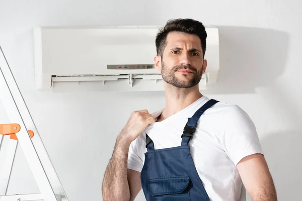 Trabajador disgustado que sufre de calor mientras está de pie cerca del acondicionador de aire roto - foto de stock