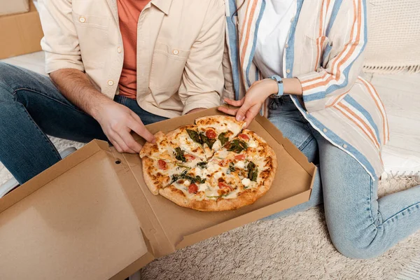 Cropped view of couple holding pieces of pizza in box on floor — Stock Photo