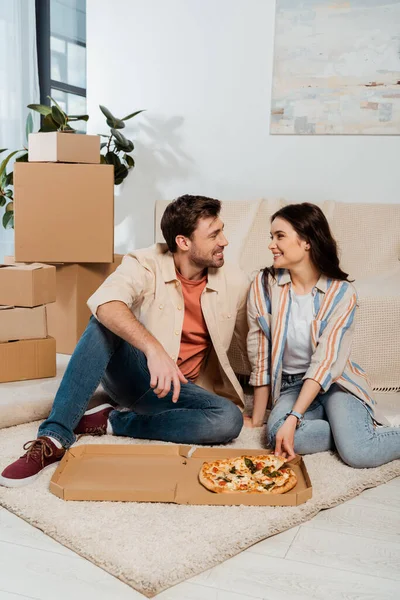 Sorrindo casal olhando uns para os outros perto de pizza e caixas de papelão no chão — Fotografia de Stock