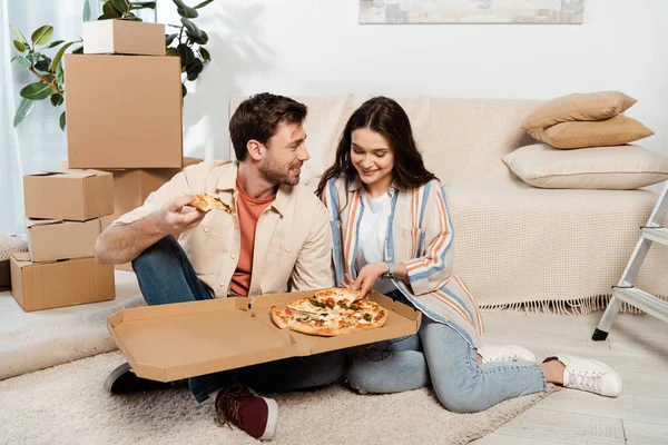 Улыбающаяся женщина держит пиццу рядом с парнем и картонные коробки на полу в гостиной — стоковое фото