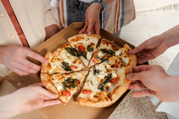 Cropped view of friends holding pieces of delicious pizza at home — Stock Photo
