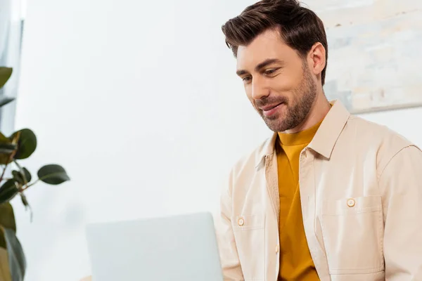 Enfoque selectivo del teletrabajo guapo usando el ordenador portátil en casa - foto de stock