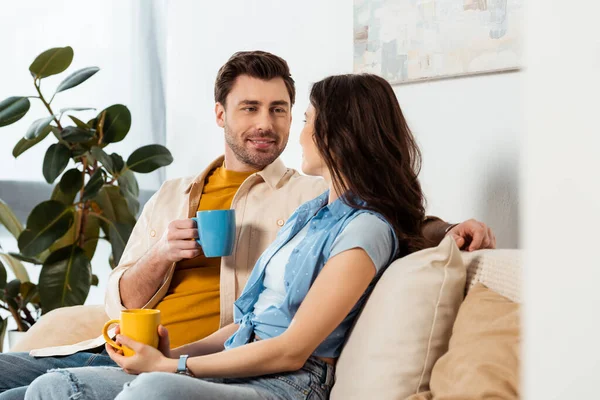 Foco seletivo de homem sorridente bebendo café perto da namorada em casa — Fotografia de Stock