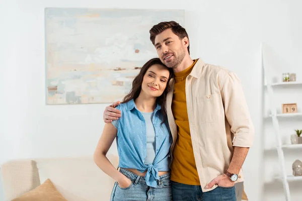 Giovane coppia sorridente via mentre abbraccia in soggiorno — Foto stock