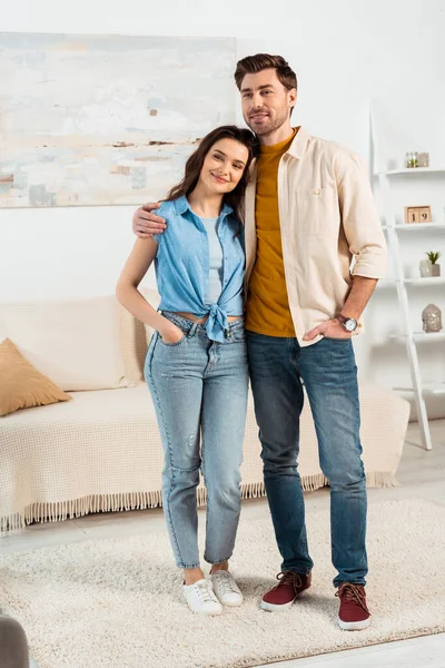 Smiling man looking away while embracing attractive woman in living room — Stock Photo