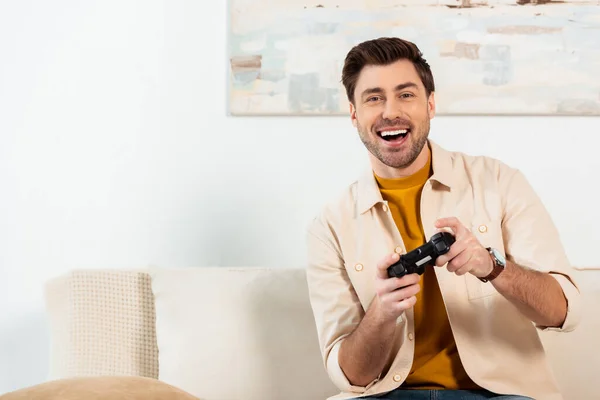 KYIV, UCRANIA - 4 de junio de 2020: Hombre alegre jugando videojuegos en el sofá en casa - foto de stock