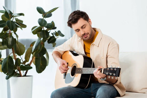 Красивый мужчина играет на акустической гитаре на диване — стоковое фото