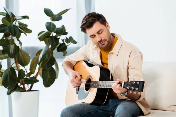 Bonito homem tocando guitarra acústica no sofá — Fotografia de Stock