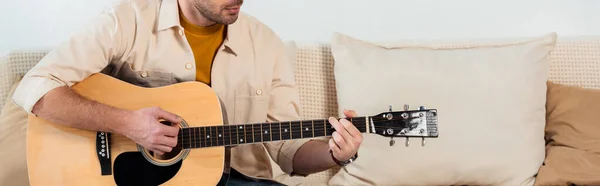 Coltivazione panoramica di giovane che suona la chitarra acustica in salotto — Foto stock