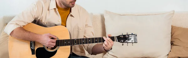 Panoramic crop of young man playing acoustic guitar in living room — Stock Photo