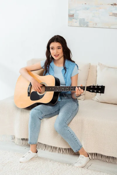 Belle femme chantant et jouant de la guitare acoustique à la maison — Photo de stock