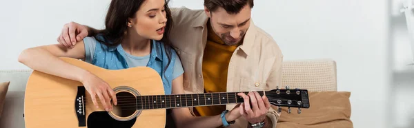 Vista panorámica del hombre enseñando a su novia a tocar la guitarra acústica - foto de stock
