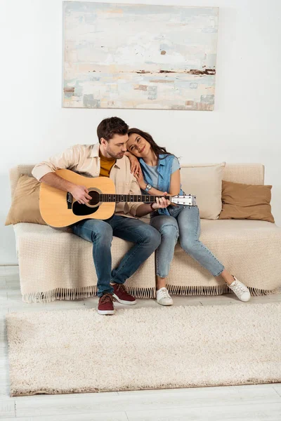 Lächelnde Frau umarmt gutaussehenden Freund, der Akustikgitarre spielt — Stockfoto