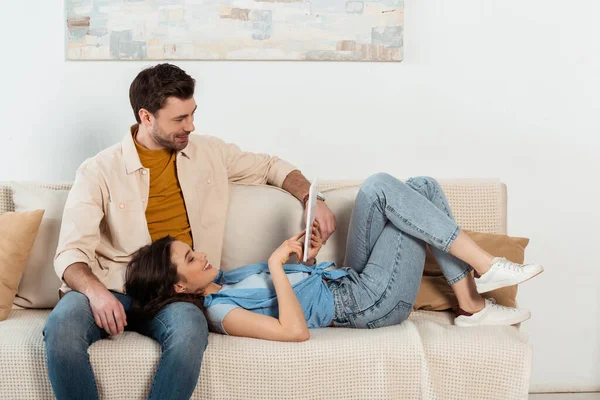 Positive Frau nutzt digitales Tablet in der Nähe ihres Freundes im Wohnzimmer — Stockfoto