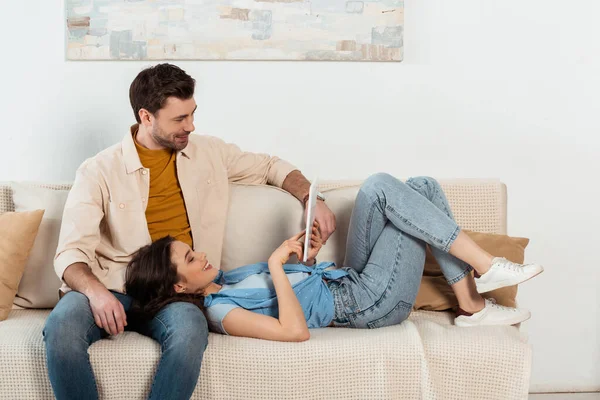 Femme positive utilisant une tablette numérique près du petit ami dans le salon — Photo de stock