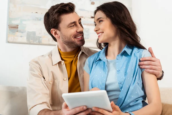 Selective focus of man hugging smiling woman with digital tablet at home — Stock Photo
