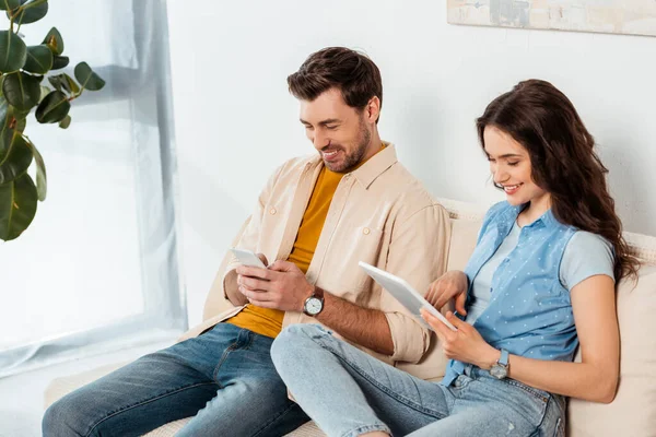 Smiling couple using smartphone and digital tablet in living room — Stock Photo