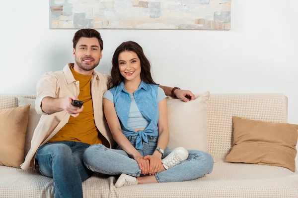 Sorrindo casal olhando para a câmera enquanto assiste tv em casa — Fotografia de Stock