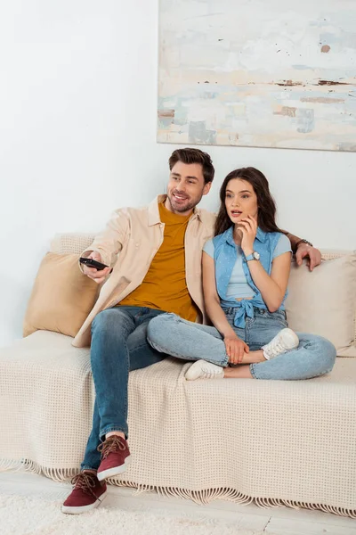 Schockierte Frau sieht Film neben lächelndem Freund auf Sofa — Stockfoto