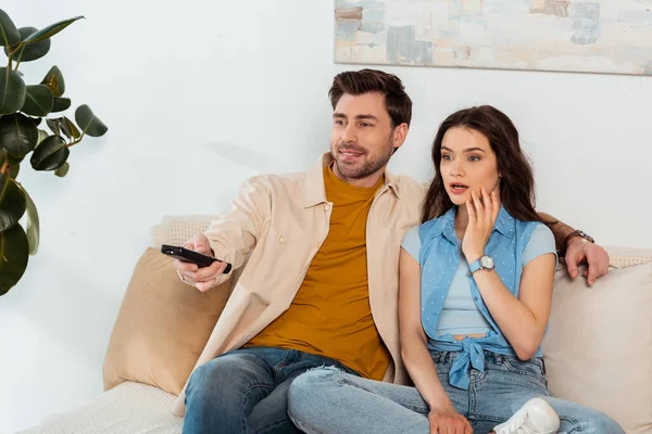 Lächelnder Mann klickt Kanäle nahe schockierter Freundin auf Couch an — Stockfoto