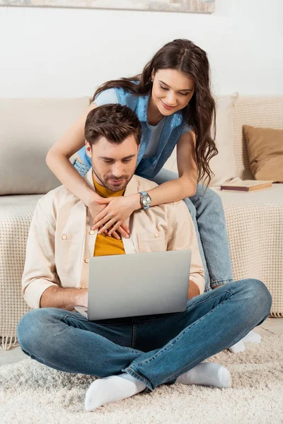 Sorrindo mulher abraçando namorado usando laptop em casa — Fotografia de Stock