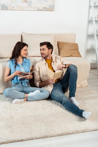 Smiling woman looking at boyfriend while reading book on carpet at home — Stock Photo