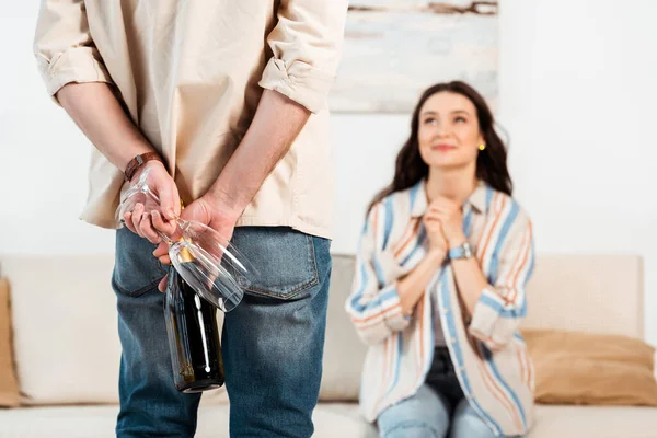 Selective focus of man hiding bottle of champagne and glasses near girlfriend at home — Stock Photo