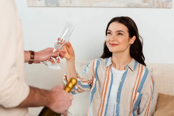 Enfoque selectivo de mujer sonriente sosteniendo copa de champán cerca de novio con botella en casa - foto de stock