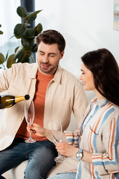 Mujer sonriente sosteniendo vidrio mientras su novio vierte champán en el sofá - foto de stock
