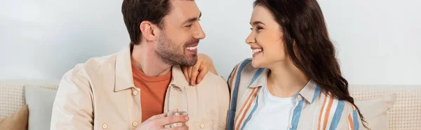 Tiro panorâmico de homem segurando copo de champanhe e sorrindo para a namorada — Fotografia de Stock