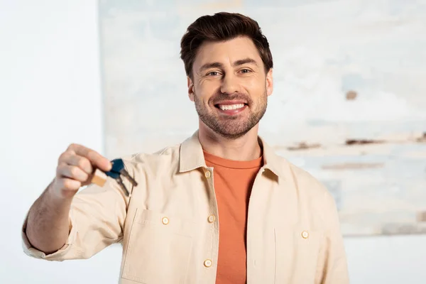 Focus selettivo dell'uomo sorridente che guarda la fotocamera mentre tiene in mano le chiavi della nuova casa — Foto stock