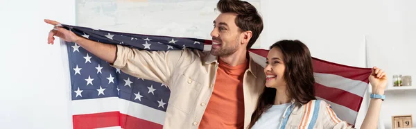 Panoramaausschnitt eines lächelnden Mannes, der mit dem Finger zeigt, während er mit Freundin amerikanische Flagge hält — Stockfoto