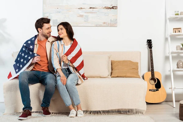 Young couple wrapping in american flag smiling at each other on couch — Stock Photo