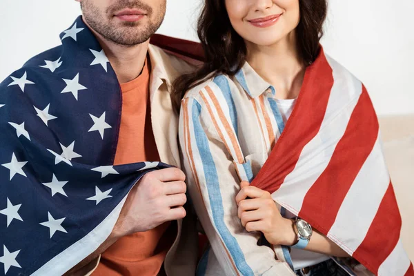 Vista recortada de mujer sonriente envuelta en bandera americana sentada cerca de novio - foto de stock