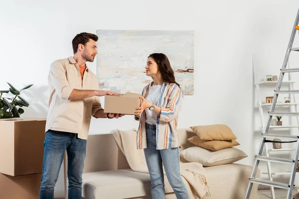 Young couple holding cardboard box near ladder in living room — Stock Photo