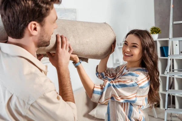 Foco seletivo de mulher sorridente segurando tapete perto do namorado em casa — Fotografia de Stock