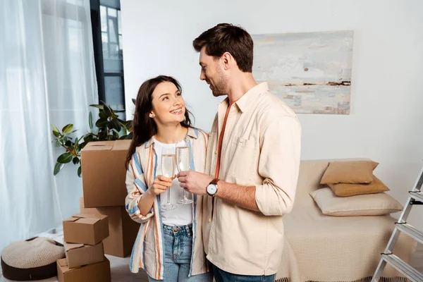 Jeune couple se souriant tout en cliquetant avec du champagne dans une nouvelle maison — Photo de stock