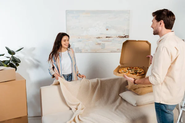 Smiling man holding pizza box near girlfriend in new house — Stock Photo