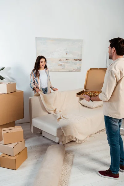 Man holding pizza box near smiling girlfriend during moving in living room — Stock Photo