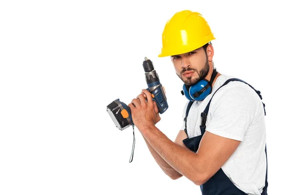 Obrero guapo en hardhat y defensores del oído sosteniendo destornillador eléctrico aislado en blanco - foto de stock