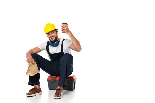 Lächelnder Bauarbeiter mit Coffee to go und Papiertüte auf weißem Hintergrund — Stockfoto