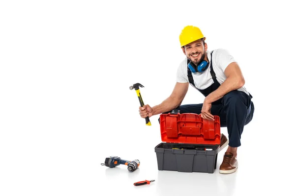 Travailleur souriant en uniforme tenant marteau près de la boîte à outils et des outils sur fond blanc — Photo de stock