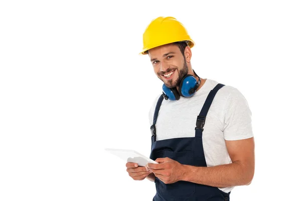 Guapo trabajador manual sonriendo a la cámara y sosteniendo la tableta digital aislada en blanco — Stock Photo