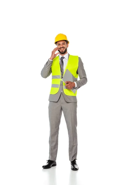 Ingeniero sonriente en traje hablando en el teléfono inteligente y sosteniendo el ordenador portátil sobre fondo blanco - foto de stock