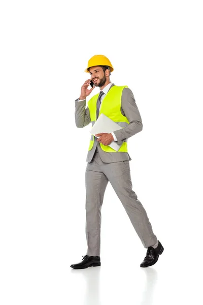 Engenheiro sorridente em hardhat e terno falando no smartphone e segurando laptop no fundo branco — Fotografia de Stock